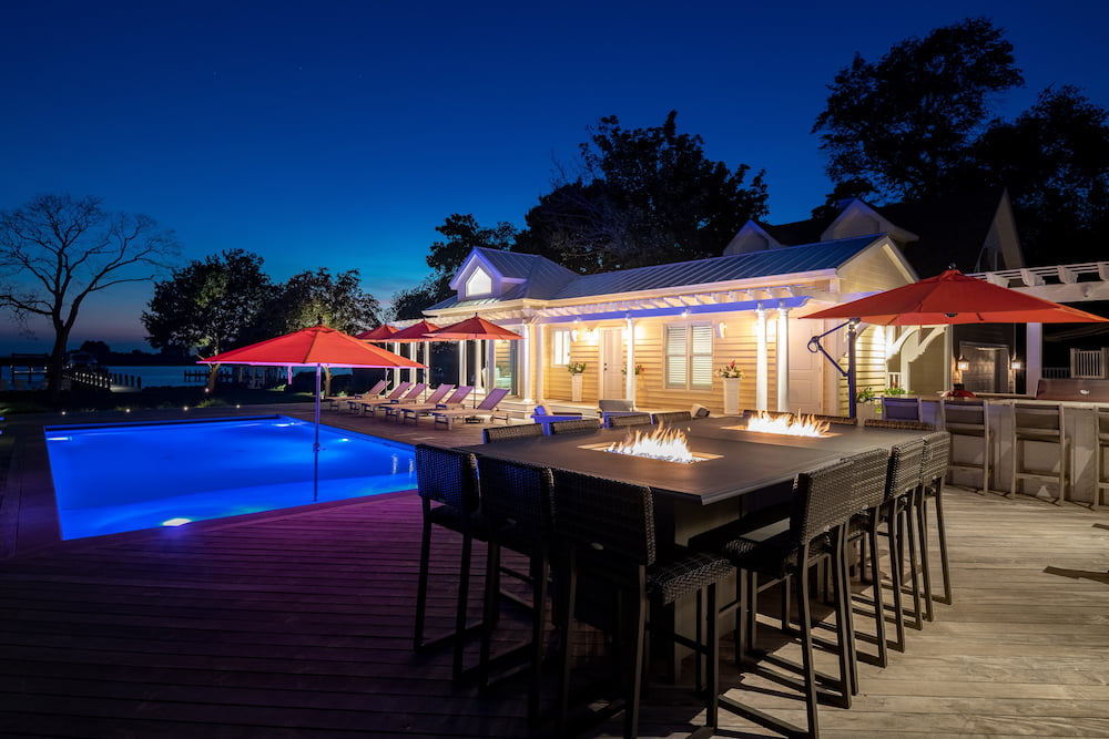 custom in-ground pool, raised fire pits, and outdoor kitchen at night