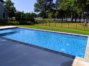 geometric pool featuring a tanning ledge next to grass area and fence