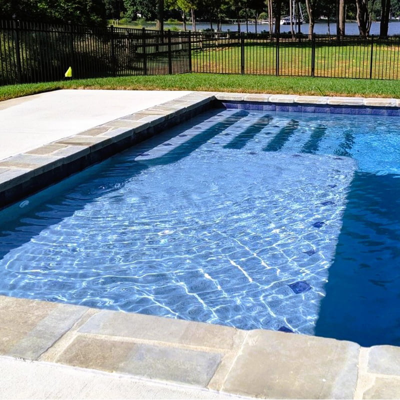 geometric pool showing large tanning ledge, stepped entry, and fencing around pool