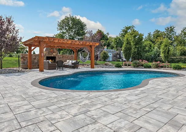 Backyard pool with stone patio, pergola, and fire pit