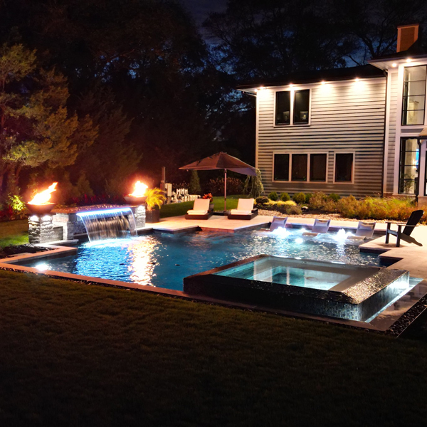 geometric pool with spa, fire features, and waterfall at night